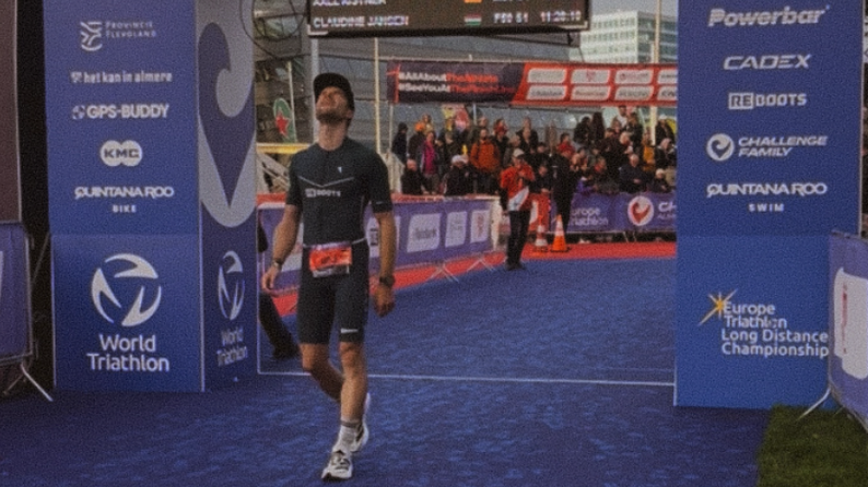 Triathlet überquert die Ziellinie bei einem Wettkampf, während Reboots als offizieller Recovery-Partner auf den Bannern sichtbar ist – Regeneration für Höchstleistungen im Ausdauersport.
