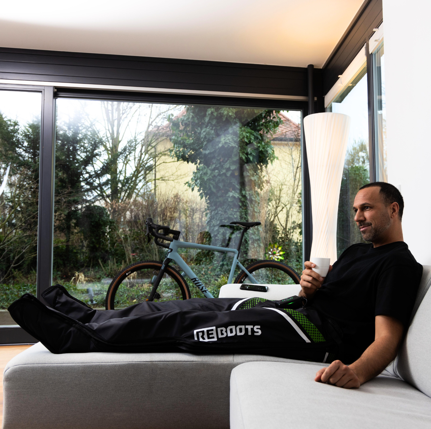 Reboots: Mann sitzt auf einem weißen Sofa und trinkt Kaffee, erholt sich nach einem Training mit GO X