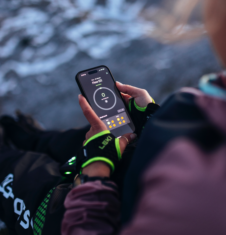 Sportlerin steuert ihre Reboots Recovery Boots über eine Smartphone-App in den Bergen – smarte Regeneration und Muskelentspannung nach intensiver Aktivität.