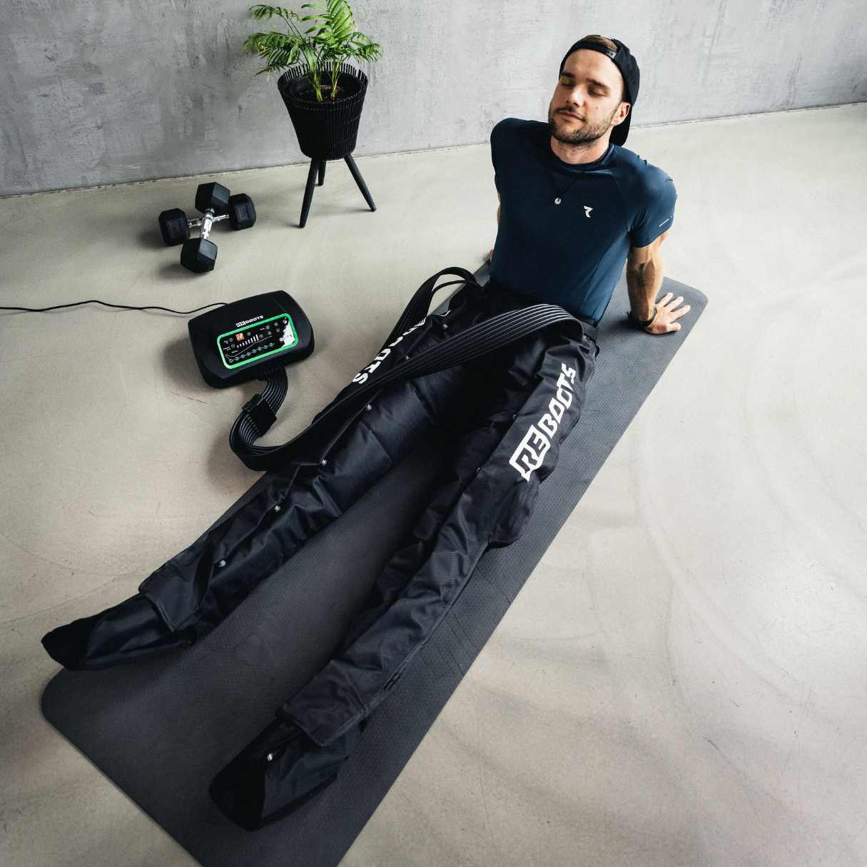 Reboots: Person, die auf einer Matte sitzt und sich zu Hause von ihrer 8-Kammer-Pressotherapie-Ausrüstung One erholt.