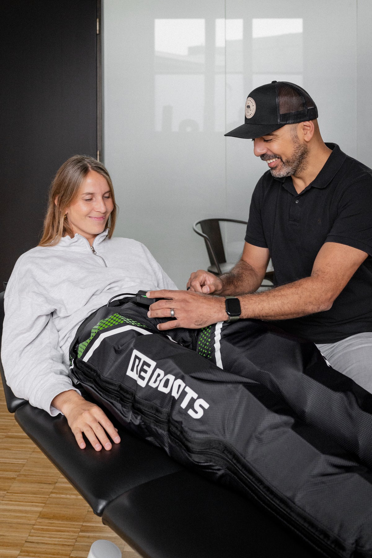 Reboots: Frau liegt auf Liege und Therapeut erklärt Kompressionsmassagegerät