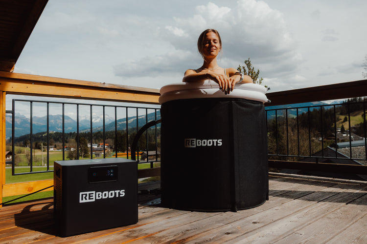 Sportlerin genießt ein Eisbad im Reboots Ice Tub mit Reboots Chiller auf sonniger Terrasse mit Bergblick – effektive Kälteanwendung zur Regeneration nach dem Training.