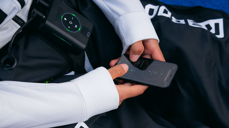 Athlet steuert Reboots Recovery Boots mit Smartphone – kabellose Kompressionsmassage für optimale Regeneration.