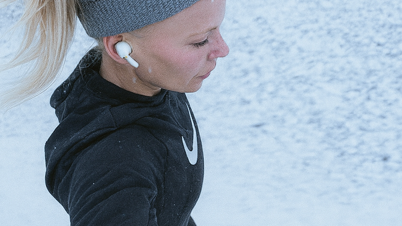 Läuferin läuft im verschneiten Wald und trainiert bei winterlichen Bedingungen mit Stirnband und Kopfhörern.