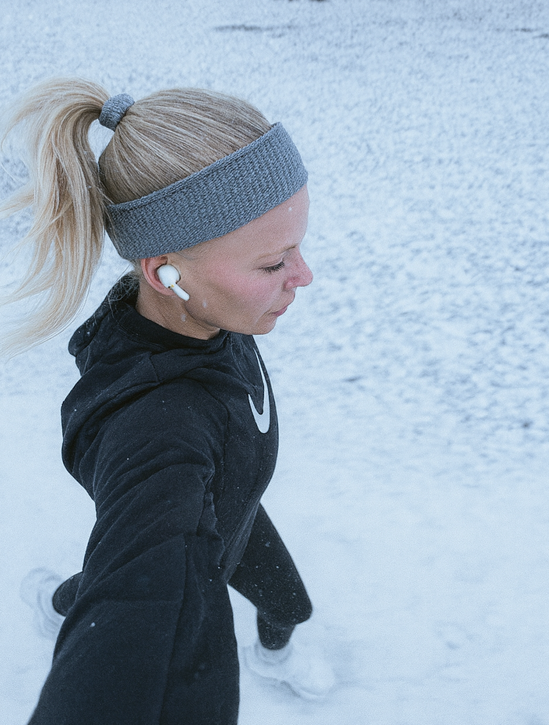Läuferin läuft im verschneiten Wald und trainiert bei winterlichen Bedingungen mit Stirnband und Kopfhörern.