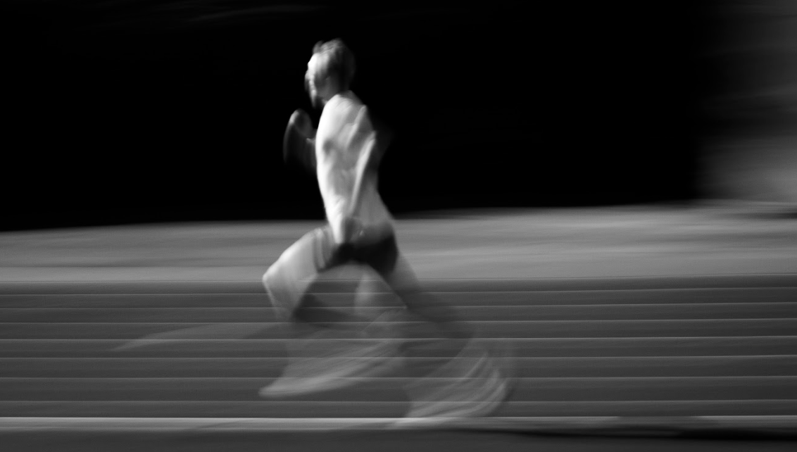 Triathlet Jonas Schomburg sprintet auf der Laufbahn – dynamische Schwarz-Weiß-Aufnahme mit Bewegungsunschärfe.