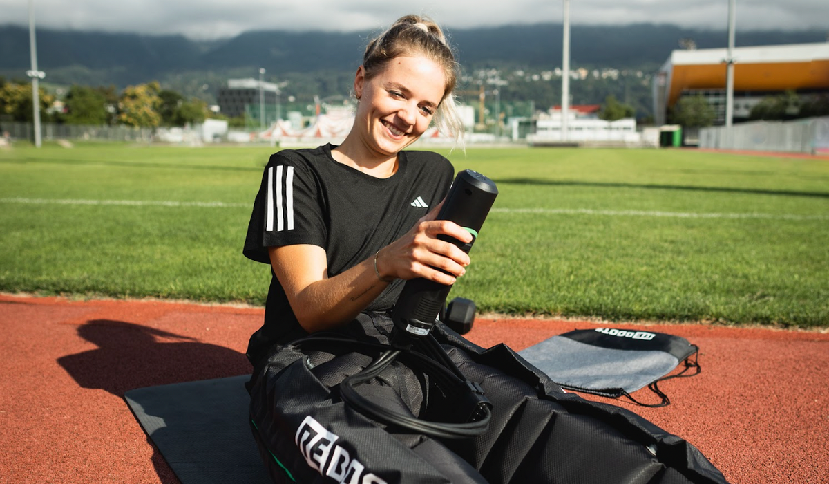 Sportlerin nutzt mobile Kompressionsmassage von Reboots zur Regeneration auf der Laufbahn
