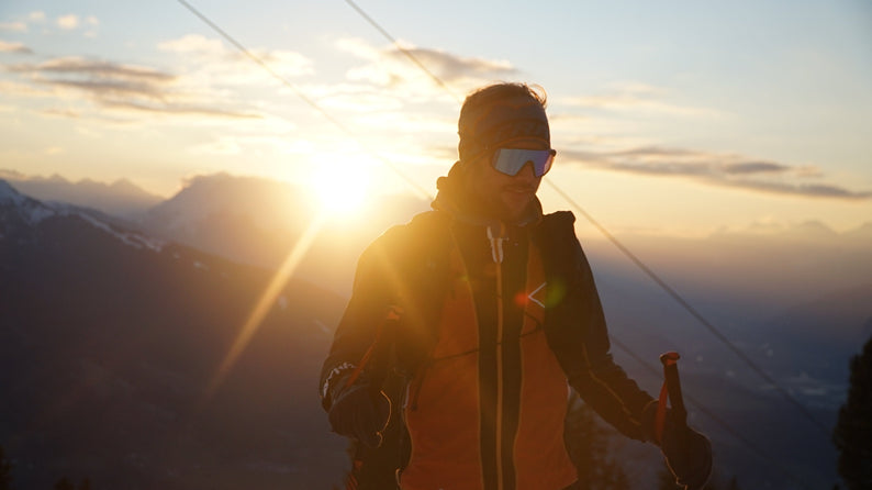 Skibergsteiger bei Sonnenaufgang in den Alpen mit Stirnband, Skibrille und Stöcken auf verschneitem Berggrat