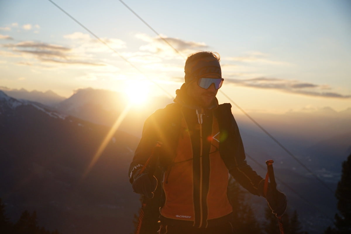 Skibergsteiger bei Sonnenaufgang in den Alpen mit Stirnband, Skibrille und Stöcken auf verschneitem Berggrat