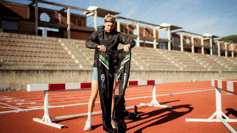 Triathlet Jonas Schomburg bereitet Reboots Kompressionsboots zur Regeneration nach dem Training auf der Laufbahn im Stadion vor.