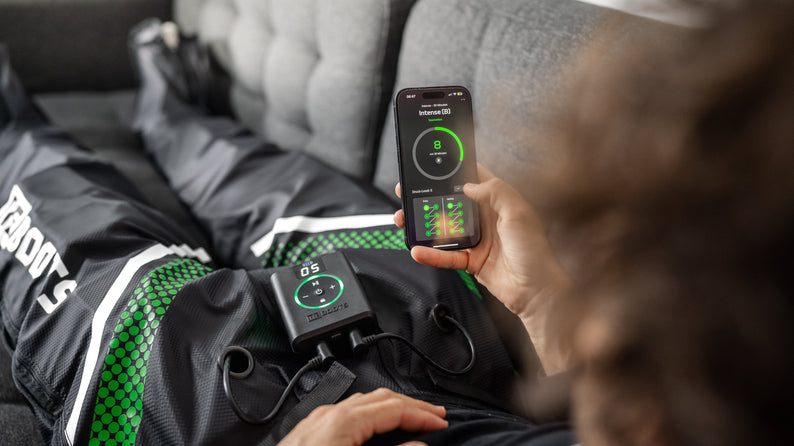 Person nutzt Reboots Kompressionsmassage mit App-Steuerung zur Regeneration auf dem Sofa