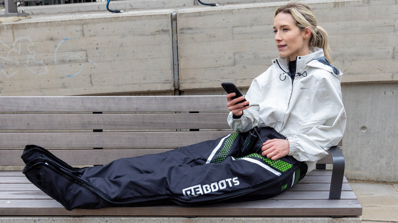 Sportlerin nutzt Reboots Recovery Boots zur Kompressionsmassage auf einer Parkbank und entspannt während der Regeneration nach dem Training.