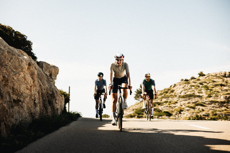 Drei Radsportler fahren gemeinsam bergauf auf sonniger Bergstraße – Reboots Athleten beim Ausdauertraining und Performance-Test unter freiem Himmel.