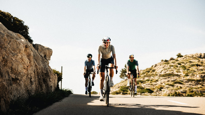 Drei Radsportler fahren gemeinsam bergauf auf sonniger Bergstraße – Reboots Athleten beim Ausdauertraining und Performance-Test unter freiem Himmel.