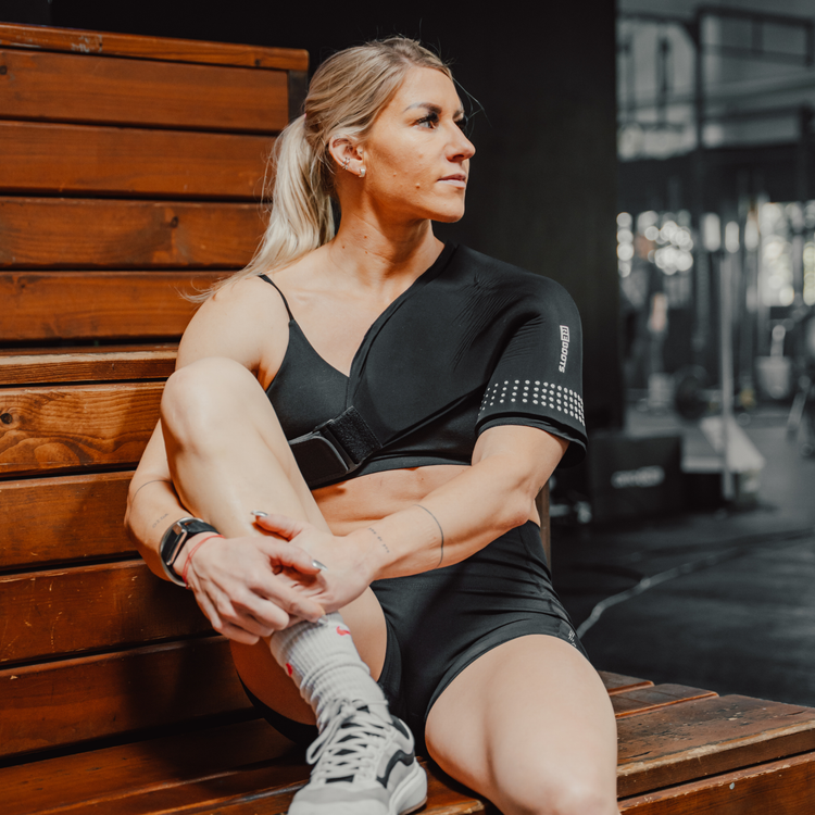 Sportlerin im Gym und nutzt Reboots Thermo Sleeve Shoulder an Schulter zur Regeneration nach dem Workout.