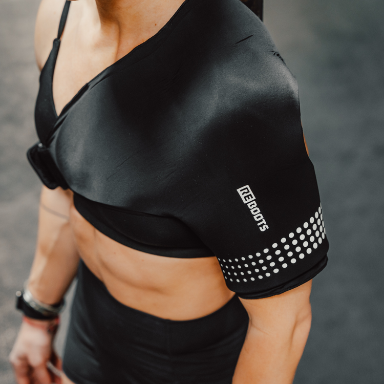Sportlerin im Gym und nutzt Reboots Thermo Sleeve Shoulder an Schulter zur Regeneration nach dem Workout.