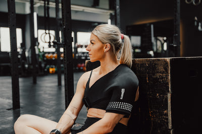 Sportlerin im Gym nutzt Reboots Thermo Sleeve Shoulder zur gezielten Wärme- und Kältehandlung und Regeneration der Schulter nach dem Training.