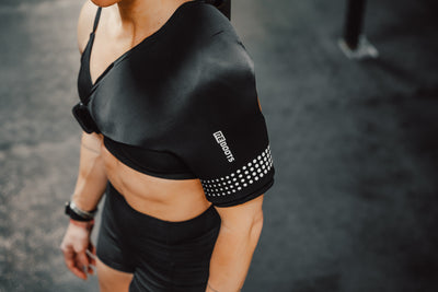 Sportlerin im Gym nutzt Reboots Thermo Sleeve Shoulder zur gezielten Wärme- und Kältehandlung und Regeneration der Schulter nach dem Training.