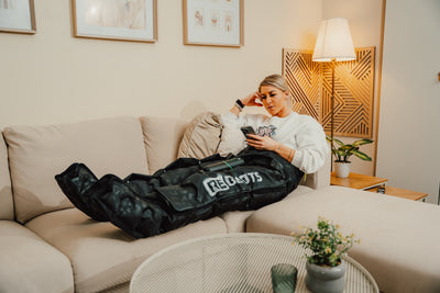Sportlerin entspannt auf dem Sofa mit Reboots Recovery Boots Limited Edition im Leo Look zur Regeneration.