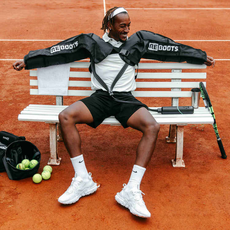 Reboots: Persona de color sentada en un banco regenerando sus brazos con la terapia de presión deportiva GO LITE.