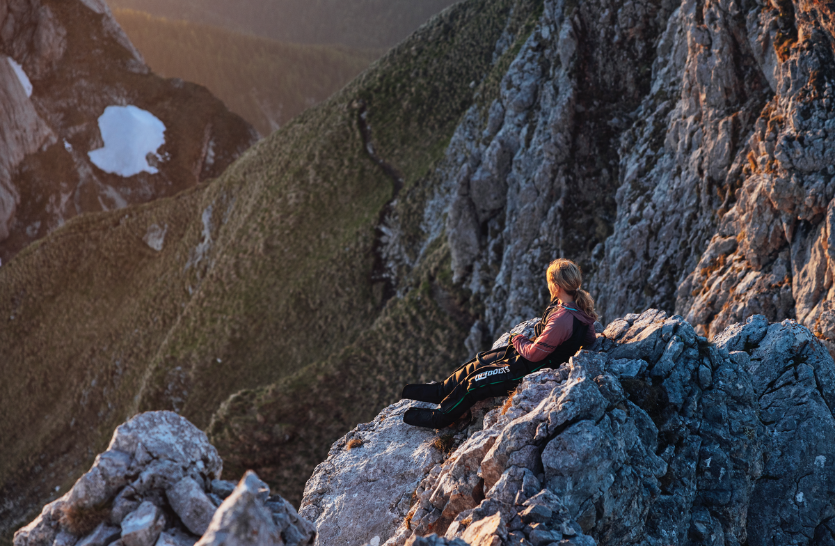 Sportlerin entspannt mit Reboots Recovery Boots auf einem Berggipfel und genießt die Regeneration nach einer Wanderung im Sonnenuntergang