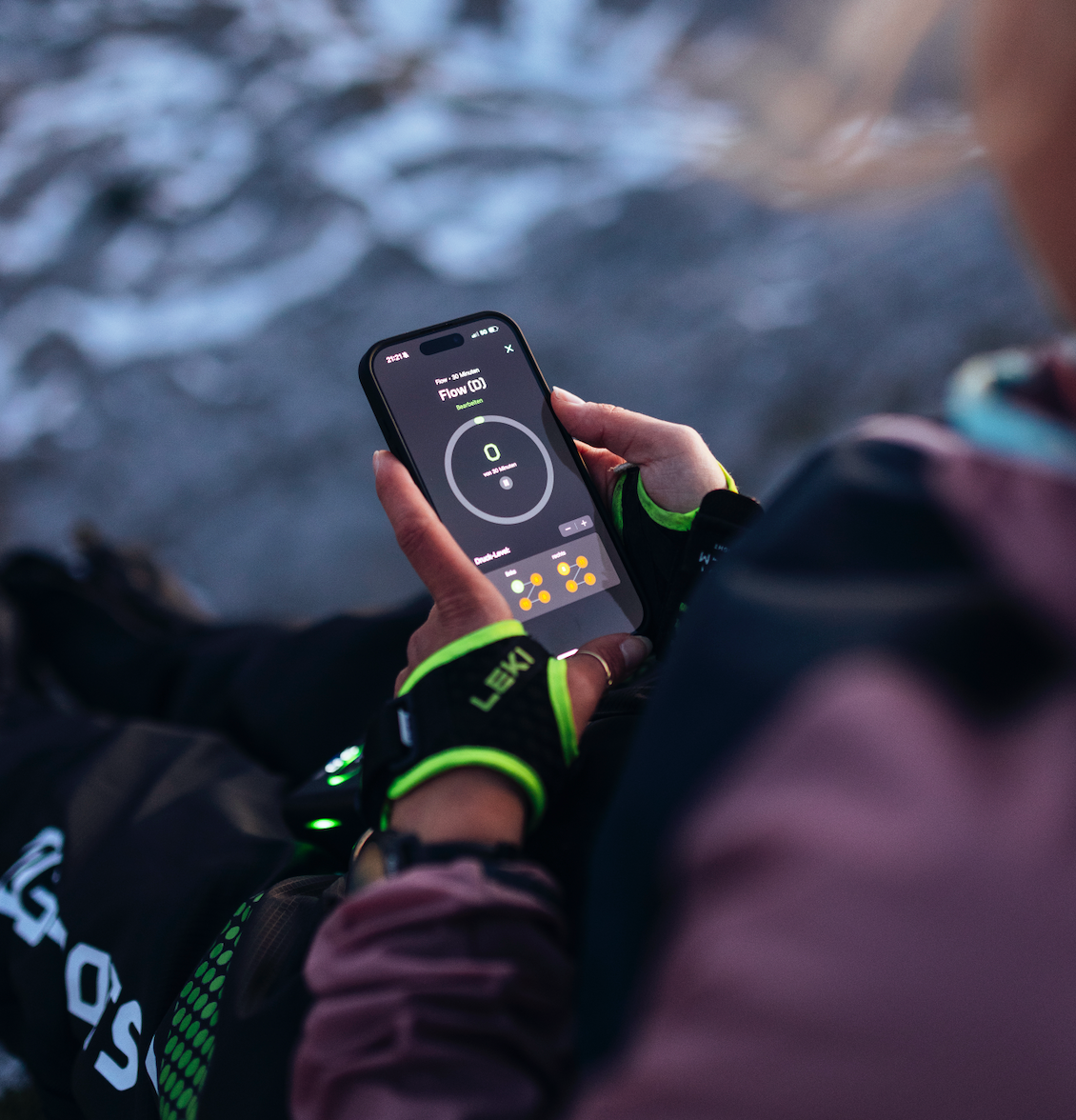 Sportlerin steuert ihre Reboots Recovery Boots über eine Smartphone-App in den Bergen – smarte Regeneration und Muskelentspannung nach intensiver Aktivität.