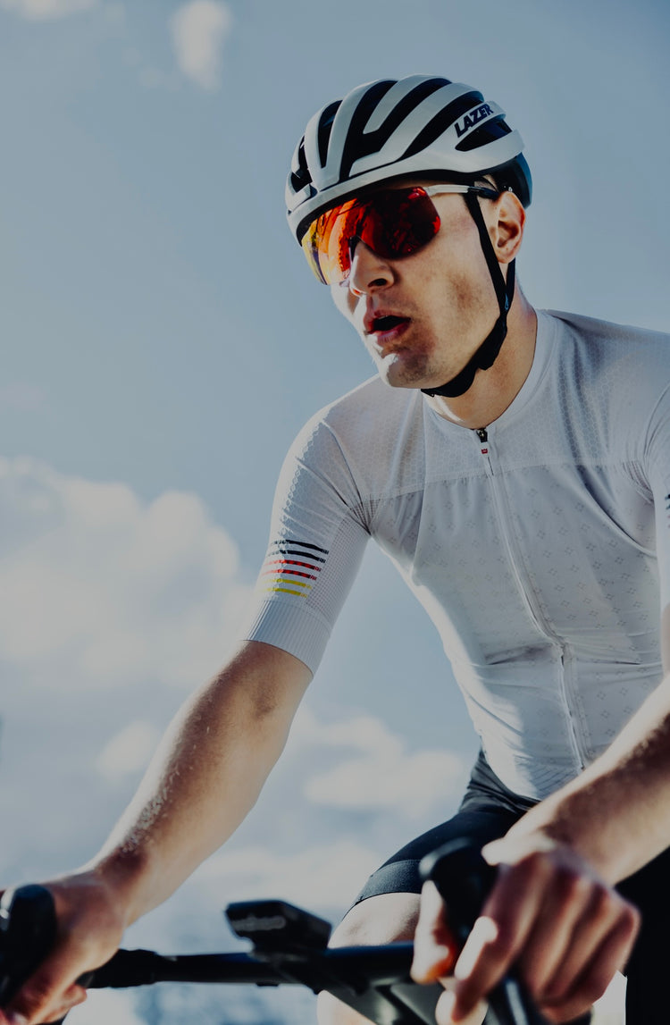 Radfahrer mit Helm und Sonnenbrille beim Training auf der Straße – Fokus auf Leistung, Ausdauer und modernes Radsport-Outfit unter blauem Himmel.