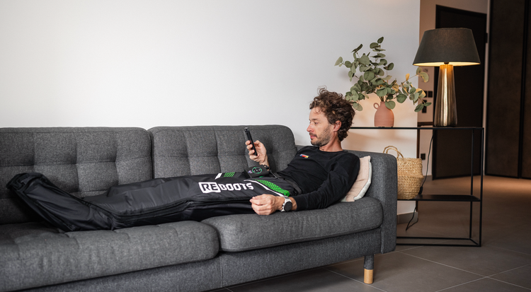 Athlet erholt sich in den Reboots Recovery Boots auf einem Sofa im Wohnzimmer. 