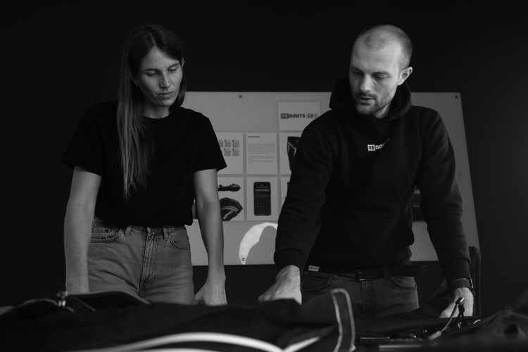 Zwei Teammitglieder prüfen Recovery Boots und diskutieren Produktdetails im Showroom mit Präsentationswand im Hintergrund