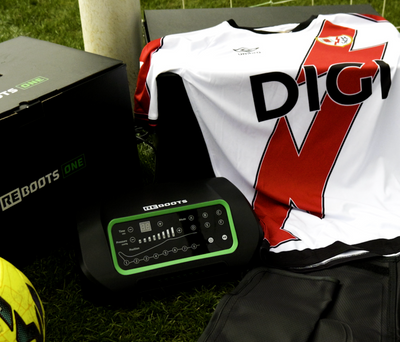 Reboots One Regenerationssystem mit Kompressionsboots, Fußballtrikot und LaLiga-Ball am Spielfeldrand für professionelle Sport-Recovery.