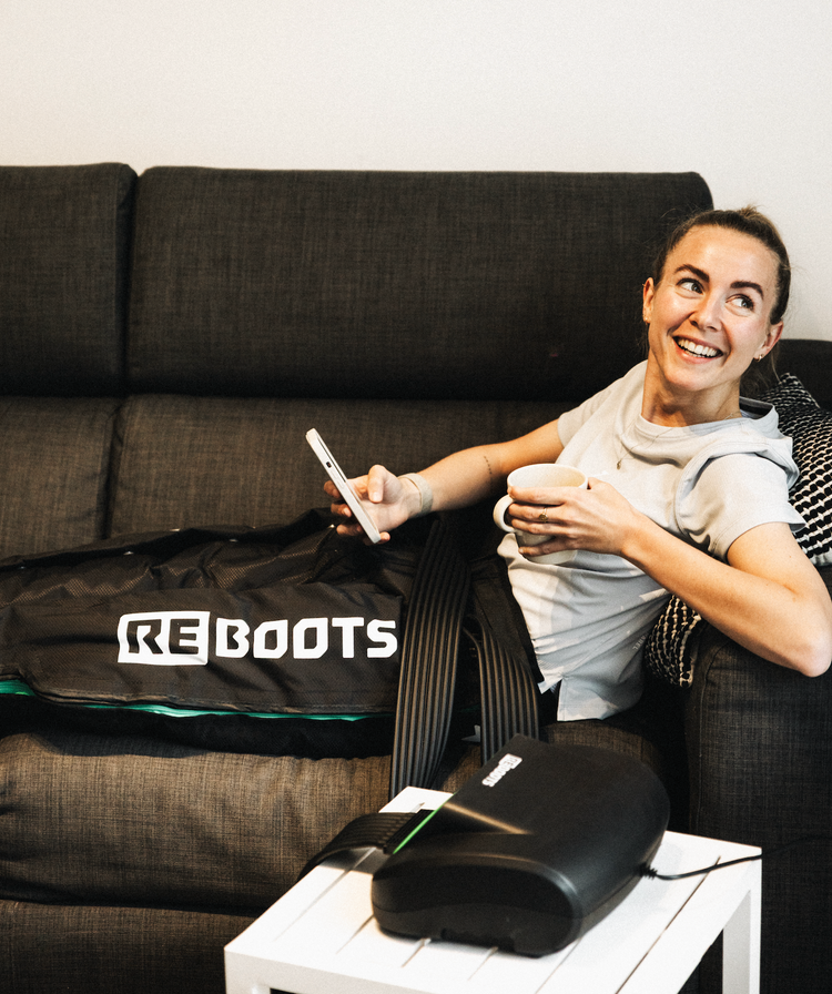 Sportlerin entspannt auf dem Sofa mit Reboots One Lite Kompressionsboots