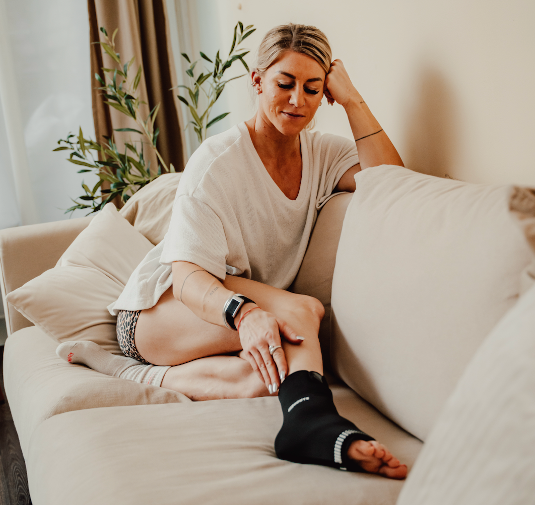 Sportlerin nutzt reboots Ankle Thermo Sleeve zu Hause auf der Couch. 