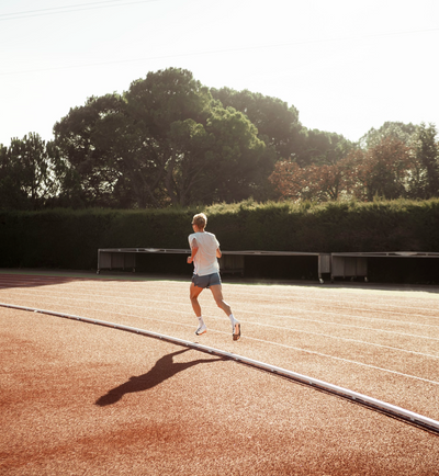 Triathlet Jonas Schomburg beim Lauftraining auf der Tartanbahn im Sonnenlicht.