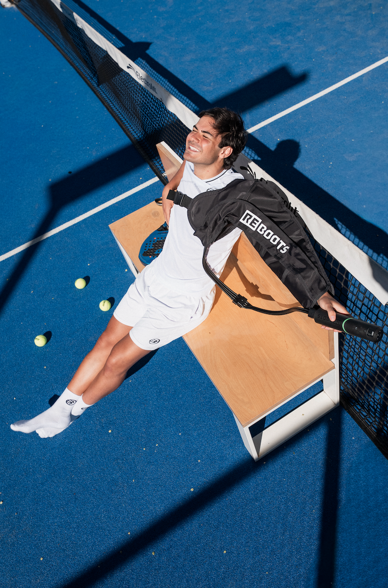 Padel-Spieler mit Reboots Kompressionsmassage zur Regeneration auf dem Padel-Court