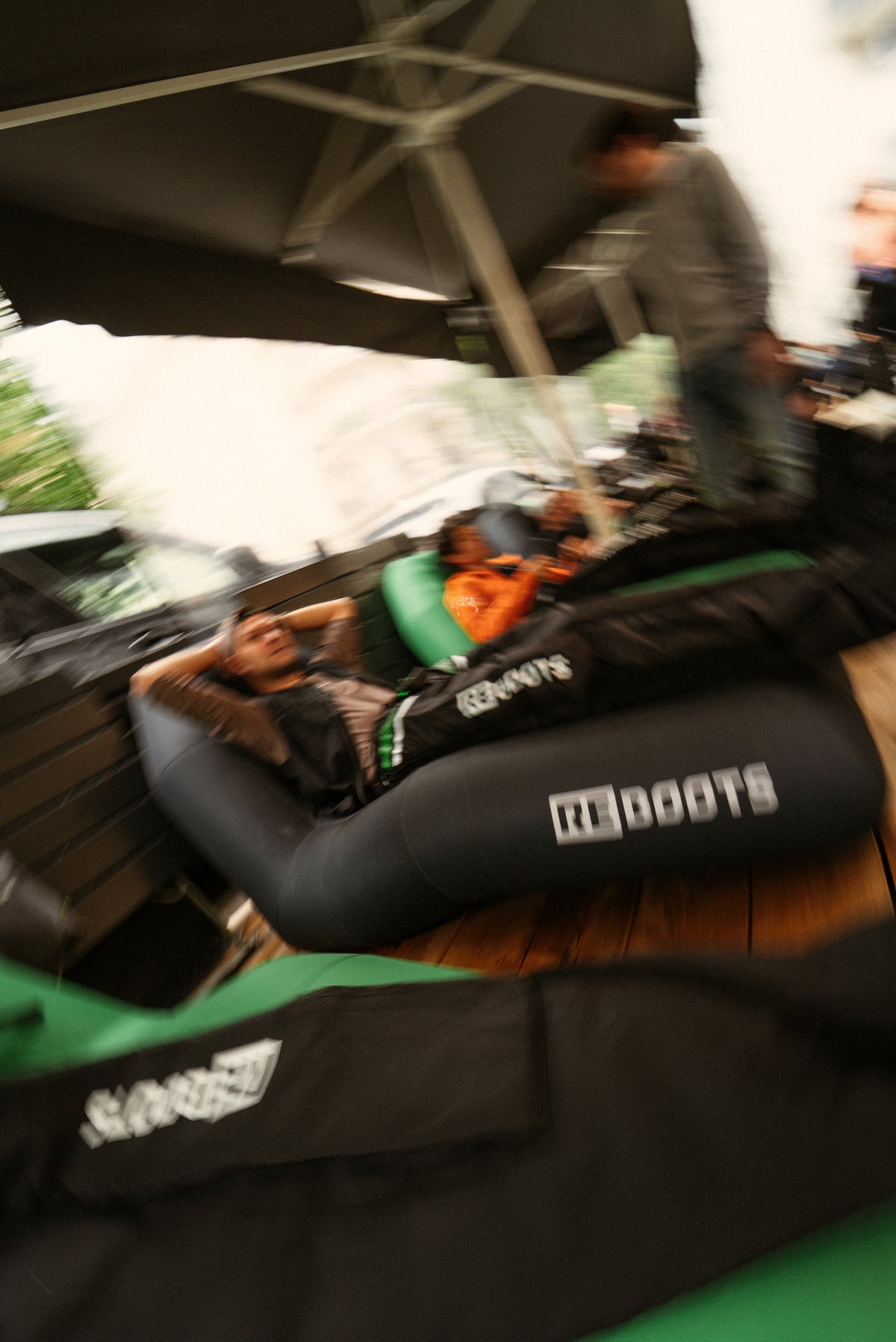 Sportler entspannen nach dem Training in Recovery Boots auf einer Terrasse unter Sonnenschirmen, Regeneration und Erholung für die Beine