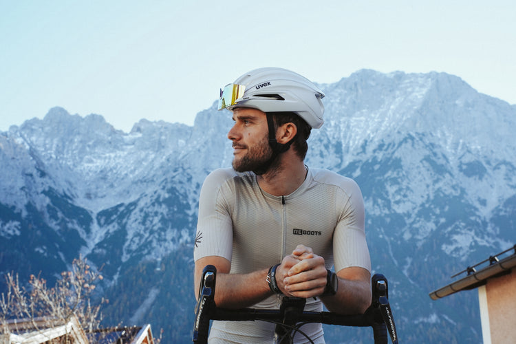 Athlet trägt Reboots Bike Jersey und Move & Recover Bib und fährt vor alpiner Bergkulisse.
