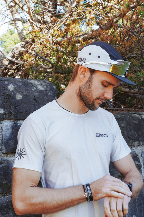 Athlet trägt das Reboots Running Jersey der Move & Recover Collection und überprüft seine Sportuhr – atmungsaktives Performance-Laufshirt in Beige