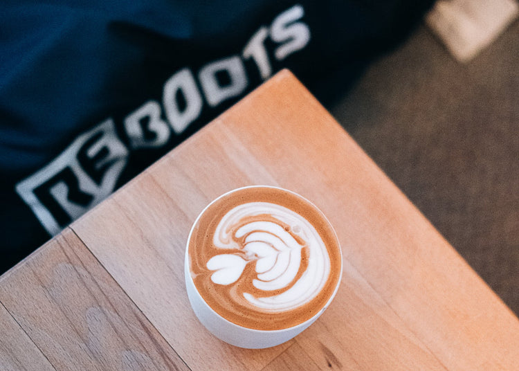 Cappuccino auf Holztisch vor Reboots Recovery Pants – entspannte Regeneration nach dem Training.