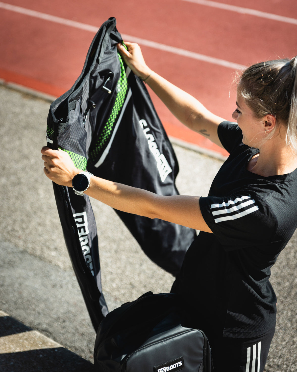 Sportlerin bereitet Reboots Recovery Boots auf der Laufbahn vor – mobile Kompressionsmassage für schnelle Regeneration nach dem Training.