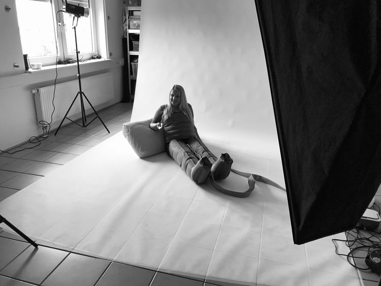 Frau sitzt im Fotostudio auf weißem Hintergrund und trägt Recovery Boots für Beinregeneration, Studiolicht und Kamera-Setup sichtbar