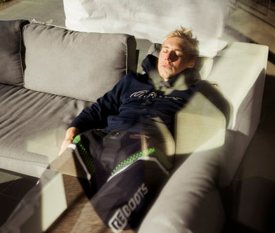 Athlet entspannt mit Reboots Kompressionsmassage zur Recovery zuhause auf dem Sofa