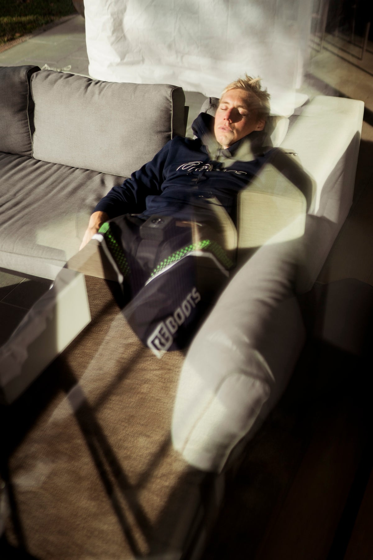 Triathlet Jonas Schomburg entspannt auf der Terrasse mit den Reboots Kompressionsmassage GO X am Bein