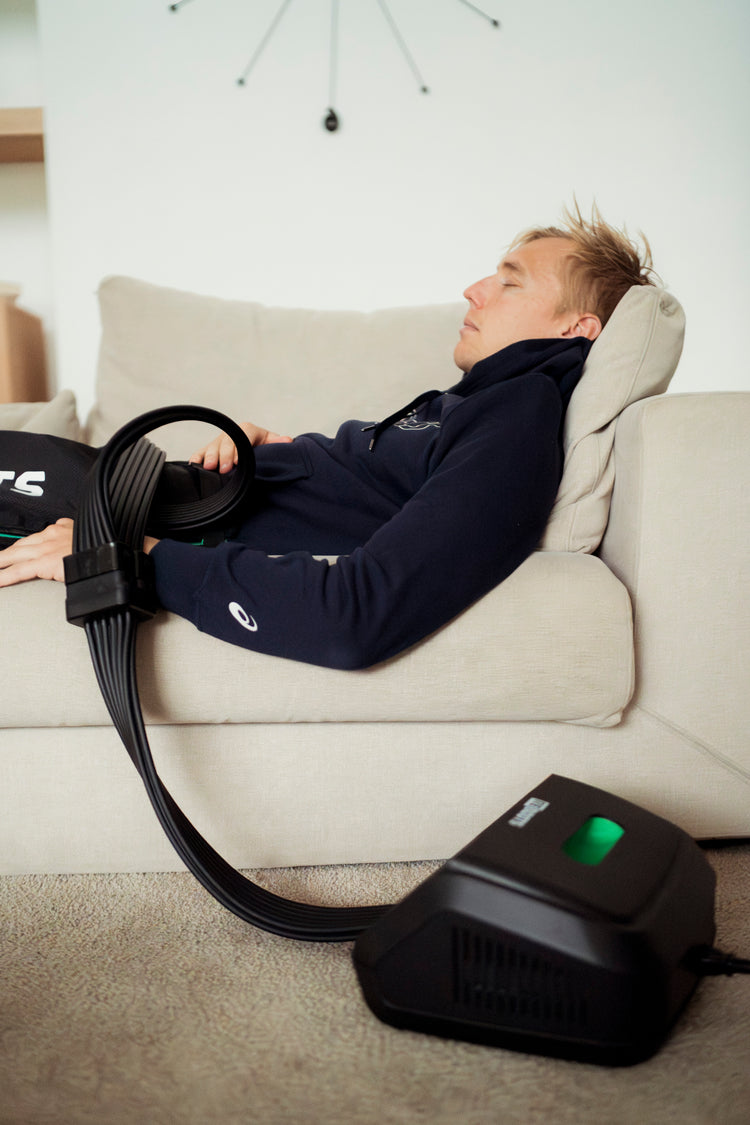Triathlet nutzt stationäres Reboots Kompressionsmassagegerät auf dem Sofa. 