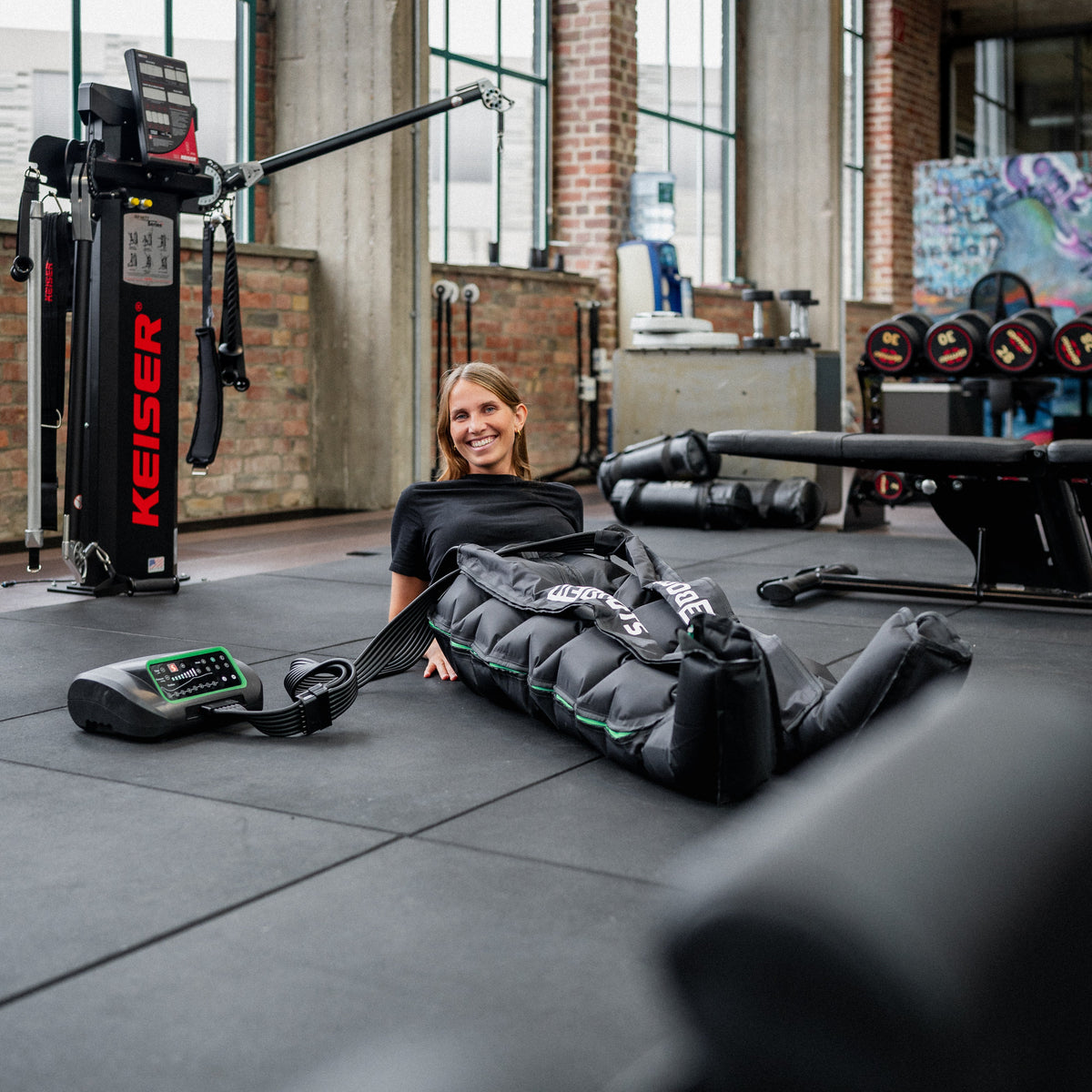 Sportlerin nutzt Reboots One Kompressionsmassagehose Reboots One Lite zur Beinregeneration im Fitnessstudio nach dem Training.