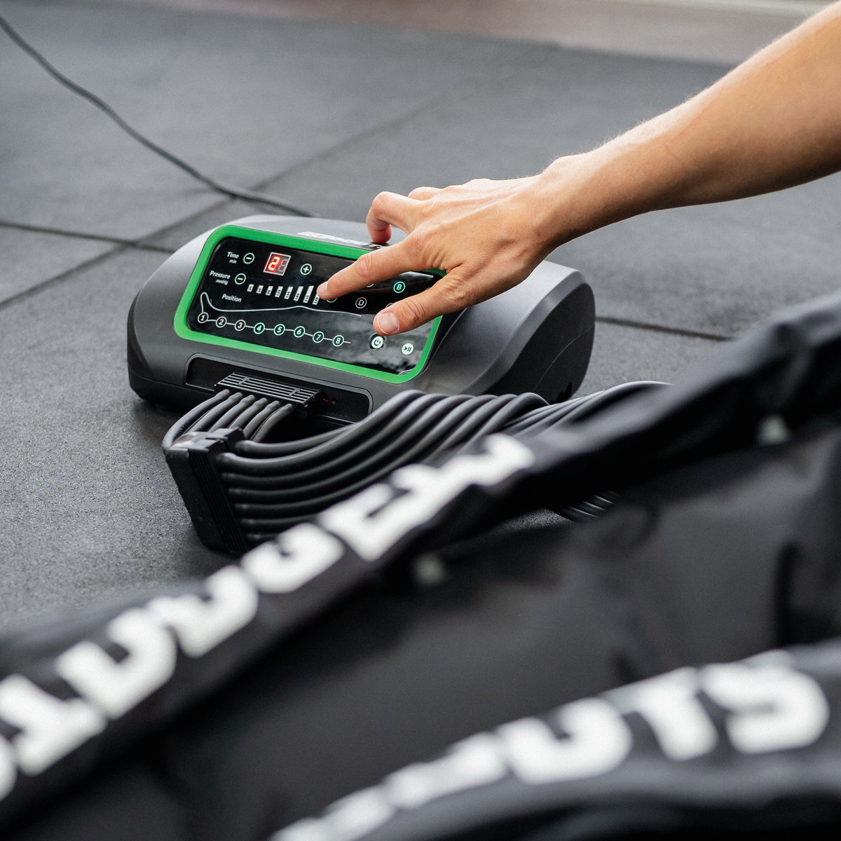 Hand stellt Reboots One Kompressionsmassagegerät reboots One Lite im Fitnessstudio ein – Steuergerät für pneumatische Regeneration der Beine.