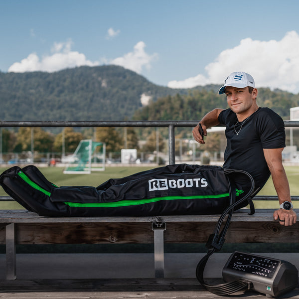 Reboots: Deportista con gorra blanca y camiseta negra, sentado en un banco recuperando con la presoterapia deportiva One Pro.