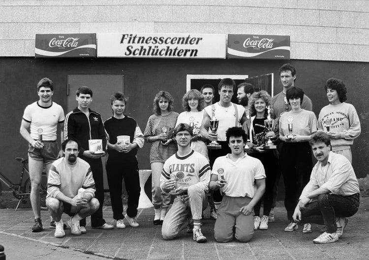 Gruppenfoto vor dem Fitnesscenter Schlüchtern in den 80er-Jahren, Sportlerinnen und Sportler mit Trainingsanzügen und Pokalen nach einem Wettbewerb
