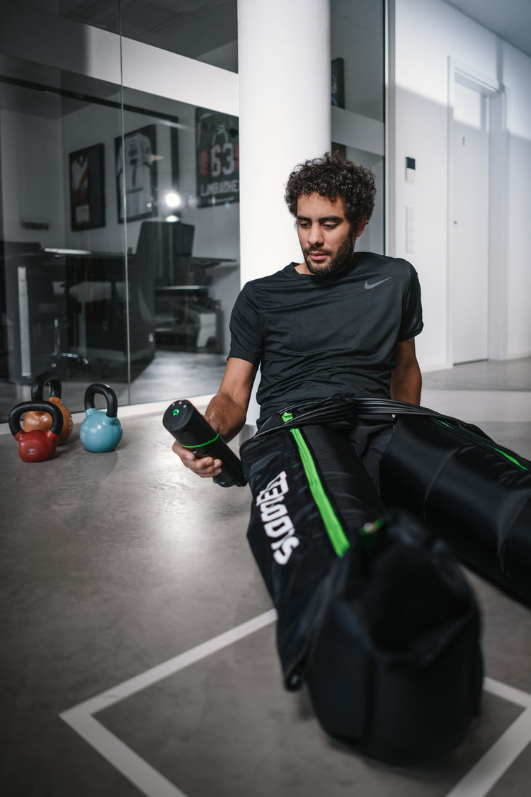 Reboots GO Lite Kompressionsboots im Gym – Sportler verwendet mobiles Recovery-System mit Akku zur schnellen Muskelregeneration nach dem Workout