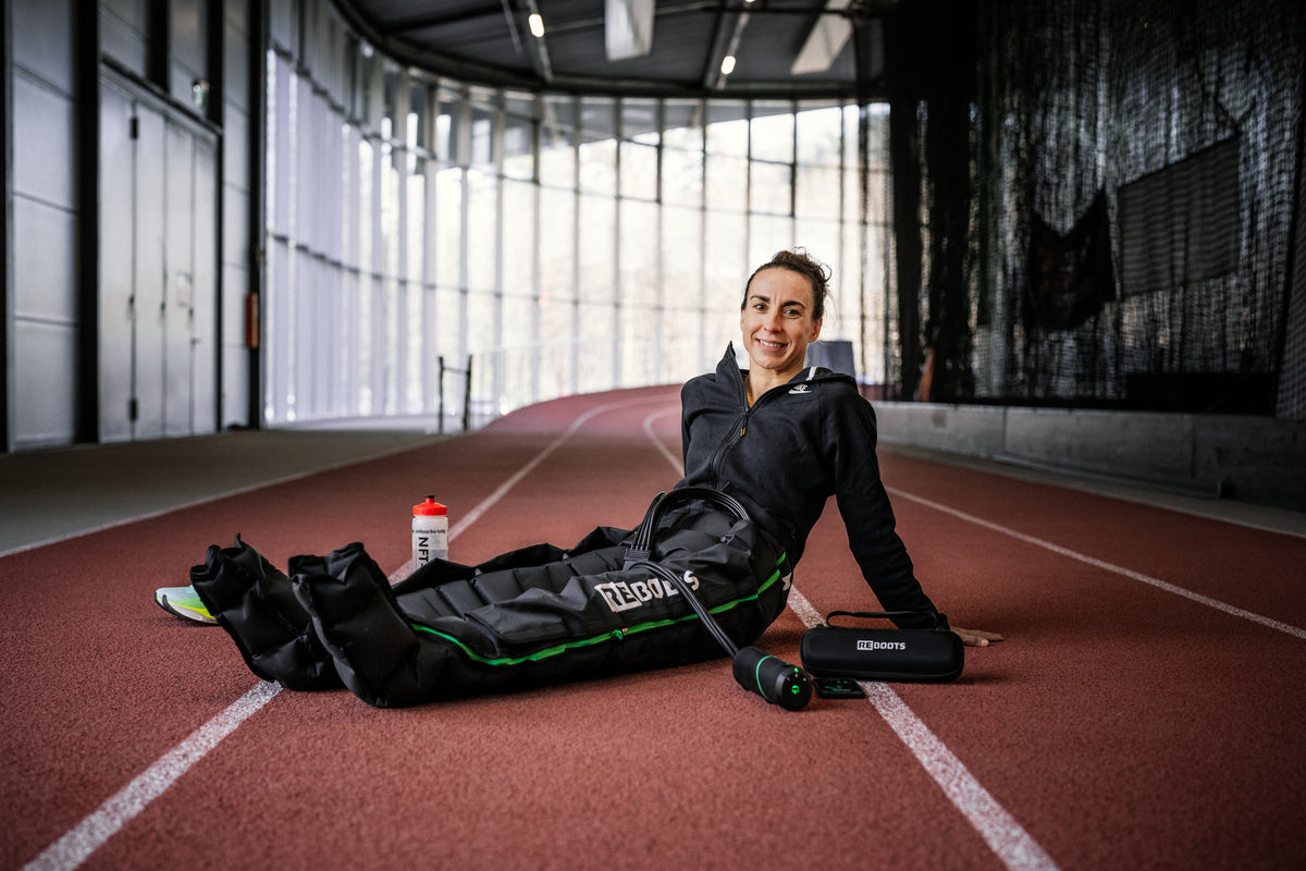 Sportlerin verwendet Reboots Recovery Boots auf der Laufbahn – flexible Regeneration für Athleten.
