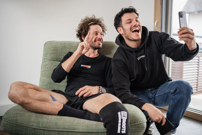 Zwei Athleten regenerieren nach dem Training mit Reboots Recovery Sleeves im Wohnzimmer